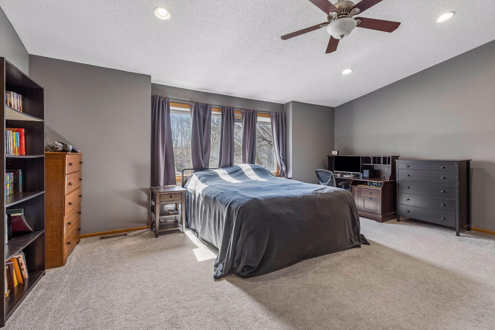 Retreat to this expansive primary suite with vaulted ceilings, plush carpet, a ceiling fan with light, a walk in closet, and four windows filling the space with natural light.