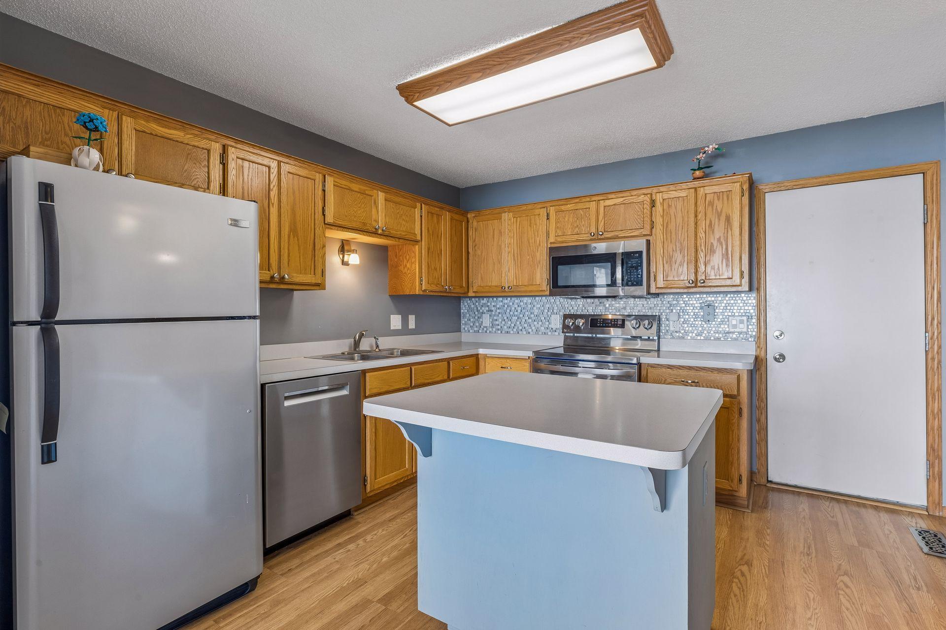 Generous kitchen featuring an island, Pergo flooring, overhead lighting, abundant cabinetry, double sink, stainless steel appliances, and convenient access to the garage.