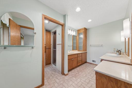 Private primary bath with custom cabinet built-ins, makeup vanity desk, double bowl back to back vanity, and pocket door to shower and commode room