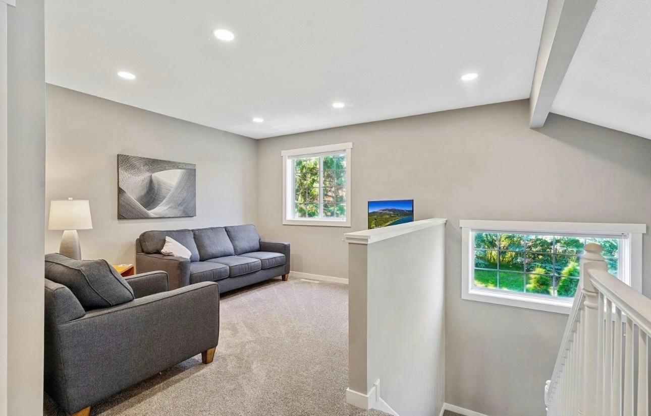 Light-filled upper-level loft featuring plush carpeting, recessed lighting, and a neutral color palette. Large windows invite an abundance of natural light, creating an airy and open atmosphere.
