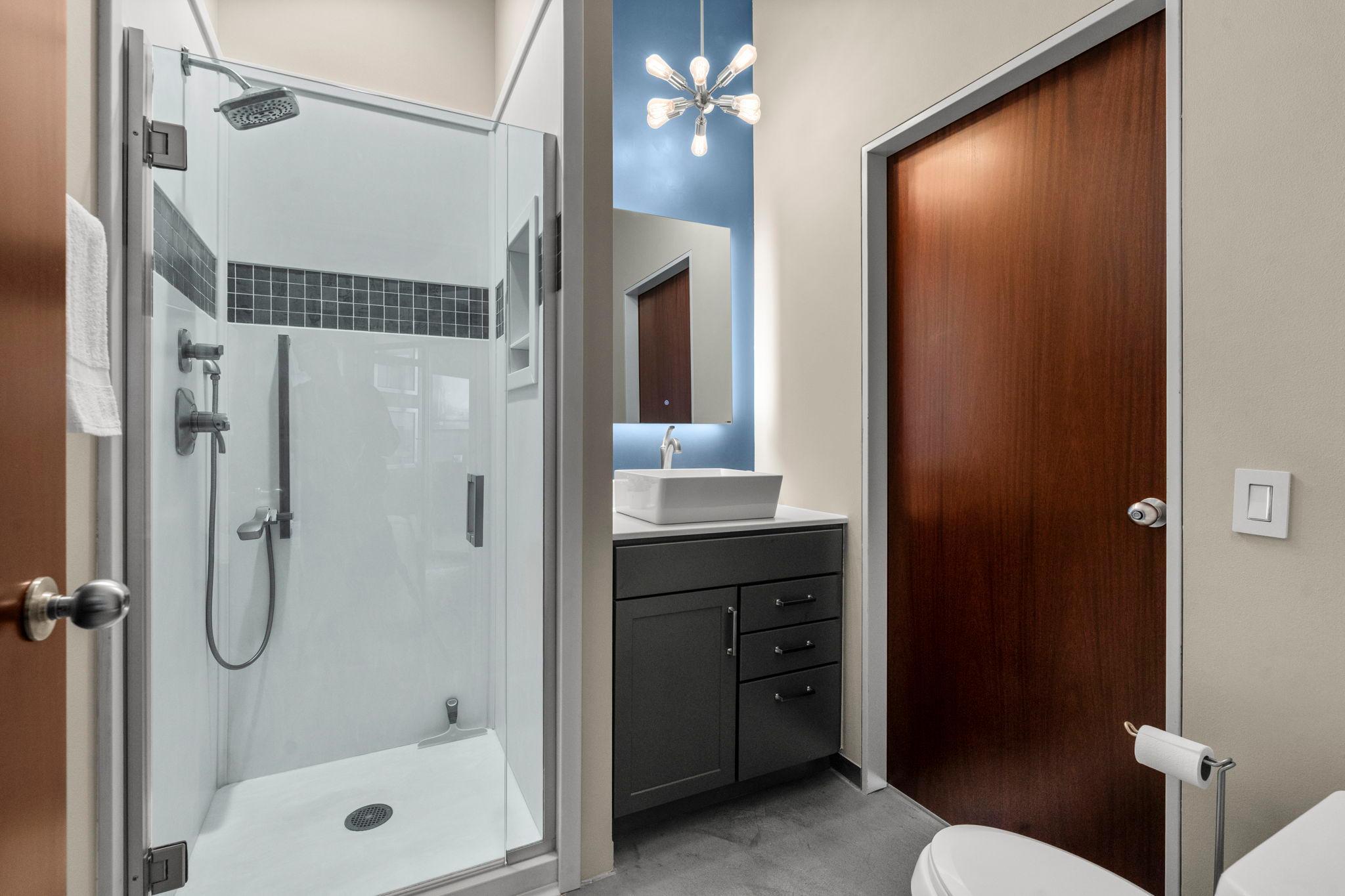 A beautifully designed bathroom showcases a walk-in tile shower paired with a backlit mirror above the sink