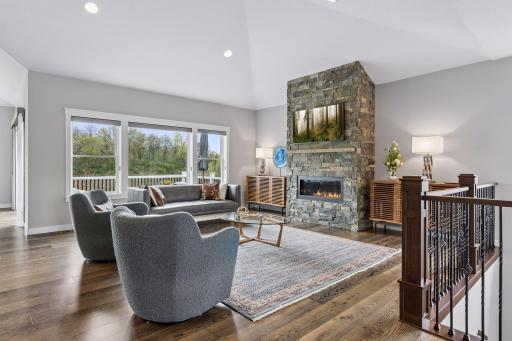 Spacious living room with vaulted ceilings, floor-to-ceiling stone fireplace, oversized windows, and beautiful backyard views. Open-concept design perfect for entertaining, relaxing, and everyday luxury living.
