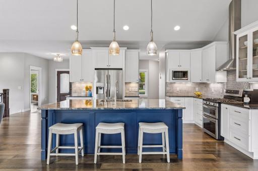 Chefs kitchen featuring a large island with seating, custom white cabinetry, stainless steel appliances, and upscale finishes. Open layout ideal for hosting gatherings and family living.