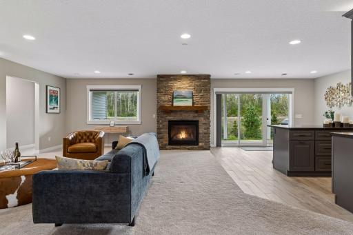 Lower-level living area with stone fireplace, soft carpeting, and walkout access to the backyard and pond views. Comfortable space for relaxing and hosting guests.