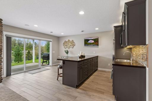 Lower-level wet bar with custom cabinetry, refrigerator, microwave and large serving counter. Perfect setup for entertaining, game nights, or guest space.