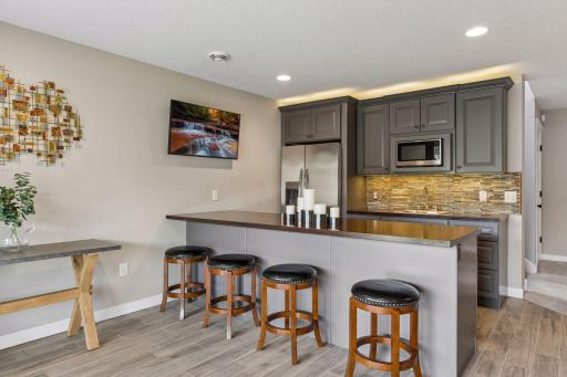 Stylish lower-level kitchenette and wet bar featuring modern cabinetry, stainless steel appliances, large peninsula seating, and functional entertainment space.