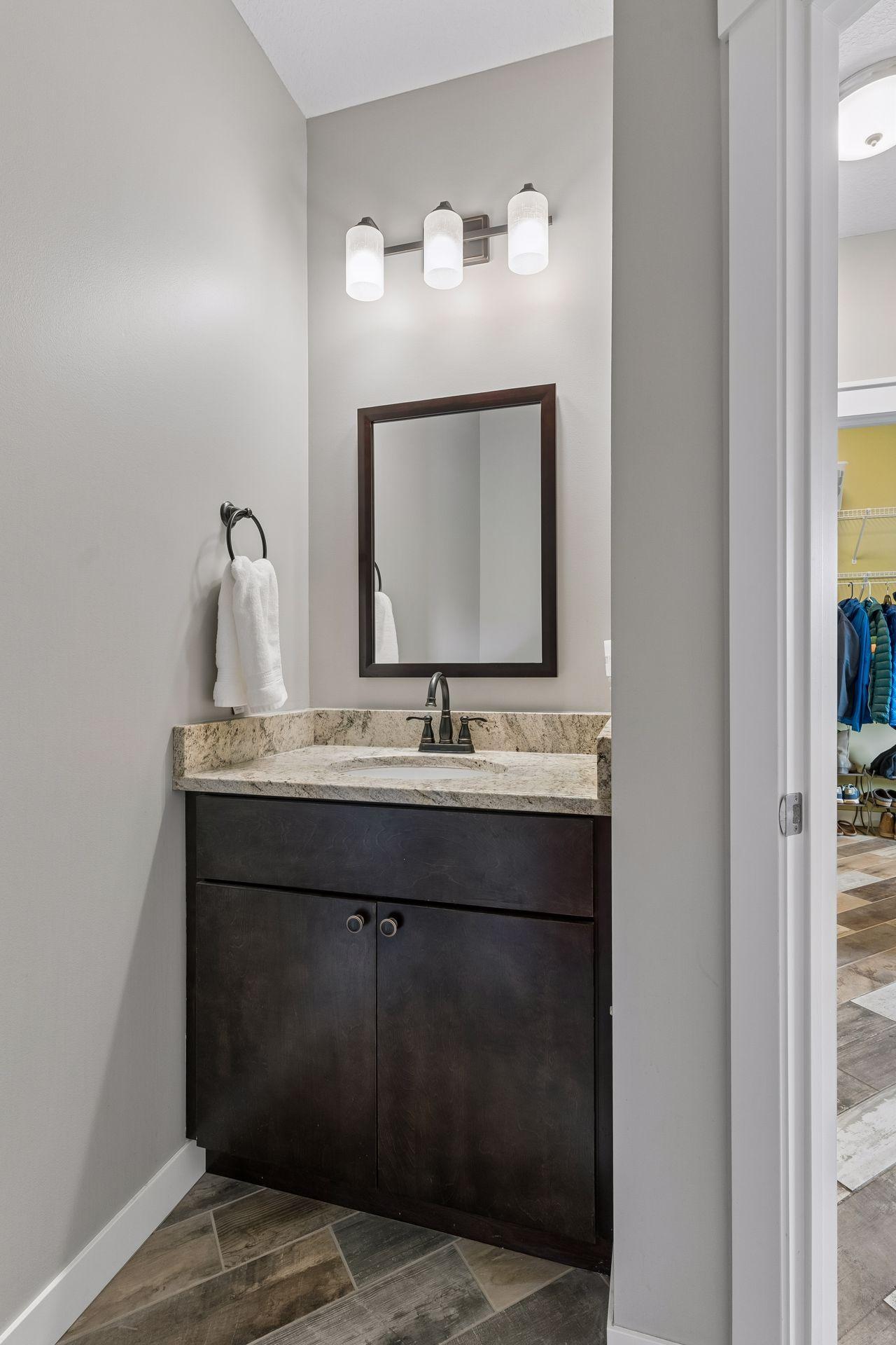 Convenient main-level half bathroom featuring granite countertop, dark wood vanity and modern fixtures. Perfectly located near the main living spaces and entry areas.