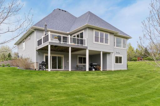 Beautiful rear exterior showcasing the maintenance-free deck, walkout lower level patio, and peaceful private backyard setting with scenic views.