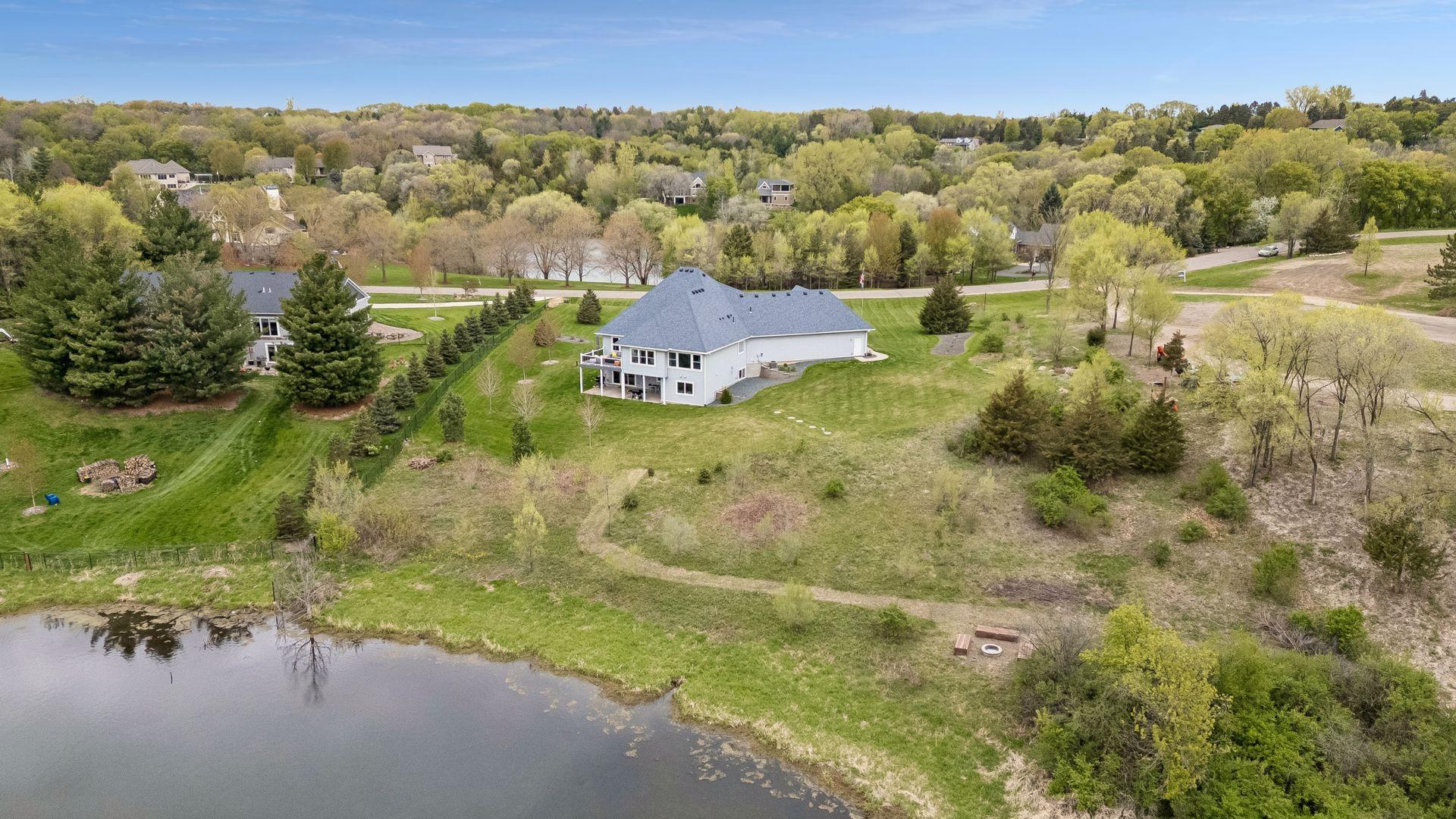 Stunning aerial view of the private acreage lot with mature trees, pond views, peaceful natural surroundings, and a fire pit area near the pond - perfect for relaxing evenings and outdoor gatherings.