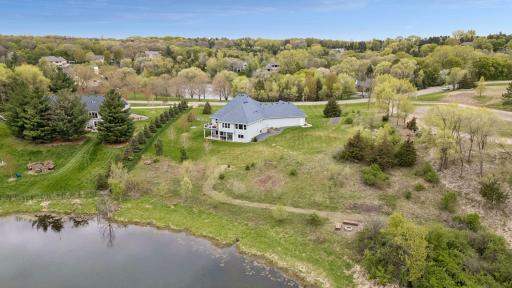 Stunning aerial view of the private acreage lot with mature trees, pond views, peaceful natural surroundings, and a fire pit area near the pond - perfect for relaxing evenings and outdoor gatherings.