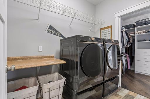 Main-level laundry room with modern washer and dryer, utility counter, extra storage space, and convenient access to the primary suite. Designed for easy one-level living.