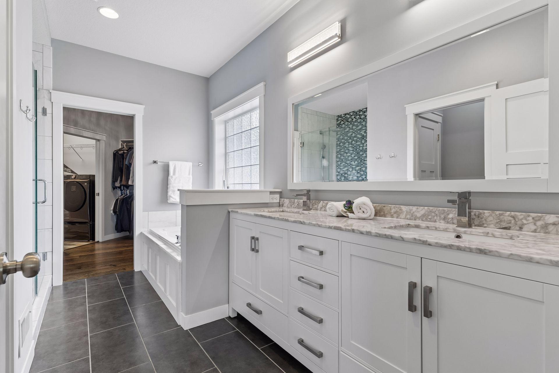 Spacious primary bathroom with dual-sink vanity, tile floors, modern fixtures, walk-in closet access, and spa-inspired design. Bright and functional luxury space.
