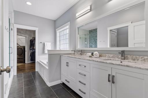 Spacious primary bathroom with dual-sink vanity, tile floors, modern fixtures, walk-in closet access, and spa-inspired design. Bright and functional luxury space.