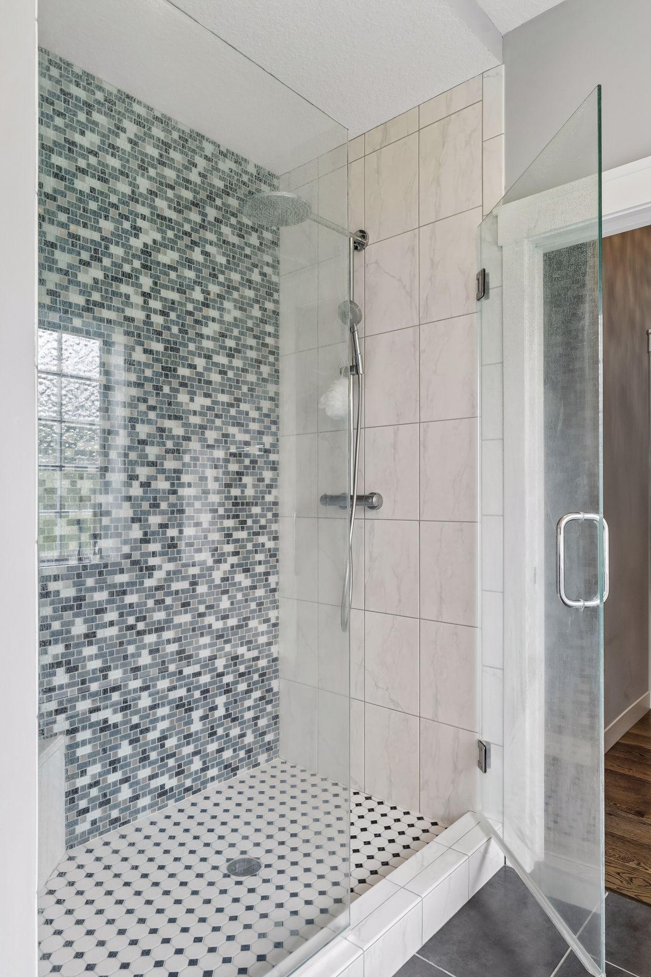 Walk-in tile shower with frameless glass door, custom tilework, rainfall shower head, and upscale finishes. Luxury spa-style bathroom with floors and modern design.