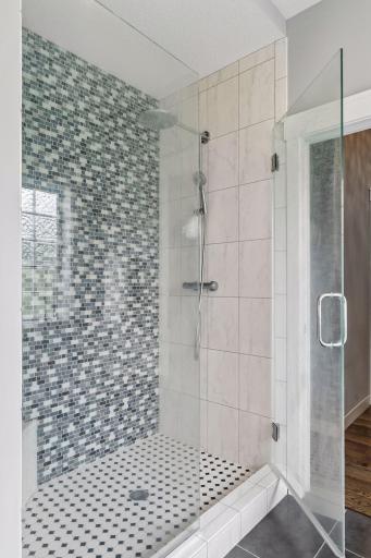 Walk-in tile shower with frameless glass door, custom tilework, rainfall shower head, and upscale finishes. Luxury spa-style bathroom with floors and modern design.
