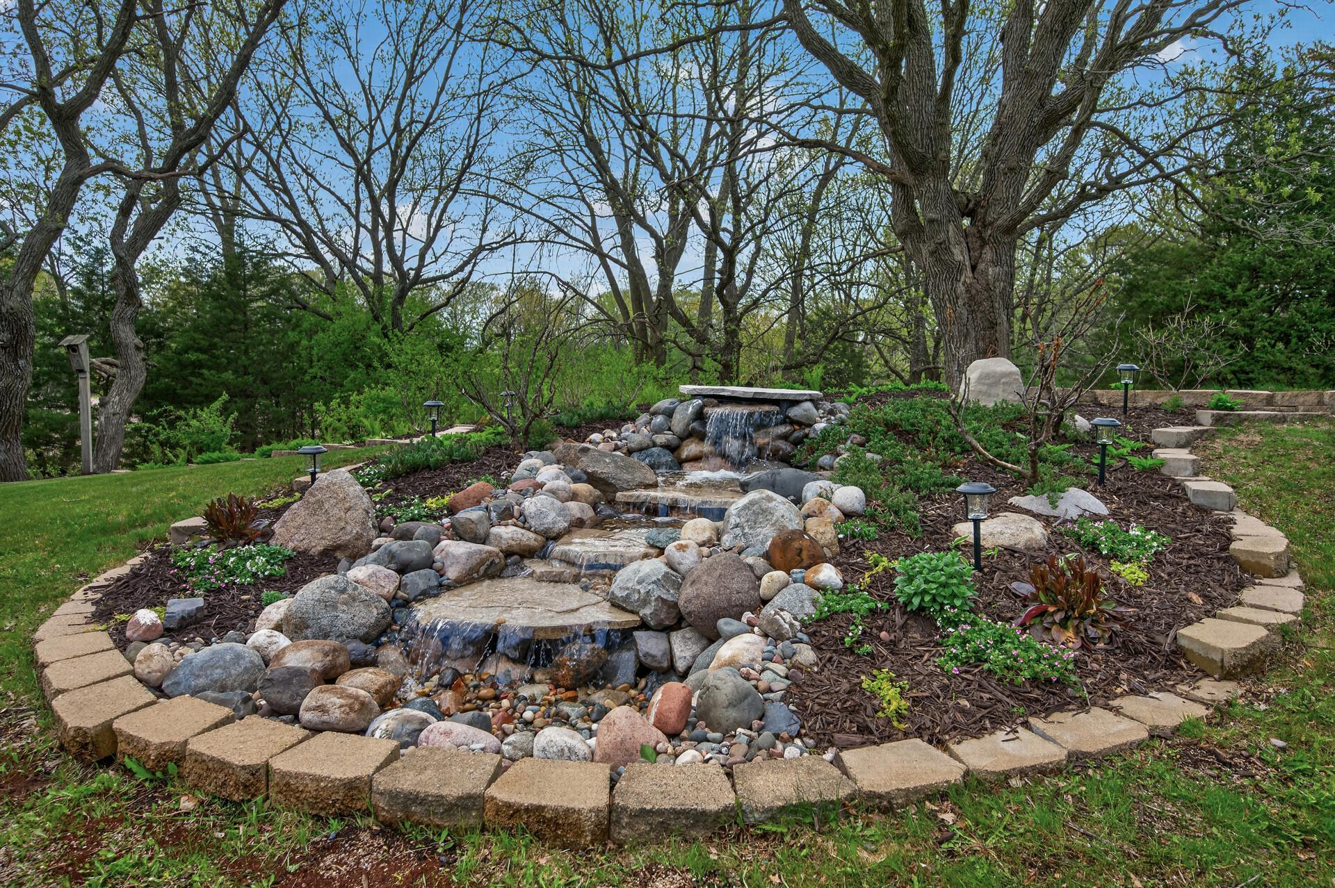 Beautifully landscaped grounds are highlighted by a serene cascading water feature, adding both charm and a peaceful ambiance to the backyard oasis.