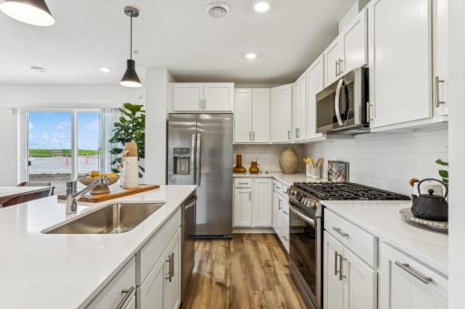 (Photo of a model home, actual homes finishes will vary) The beautiful kitchen has sleek white cabinets, SS finish appliances, luxury vinyl planking, tons of lighting and natural light as well as an island.