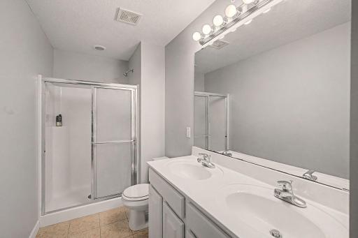 Private primary bathroom with tiled floors, dual sinks and shower.