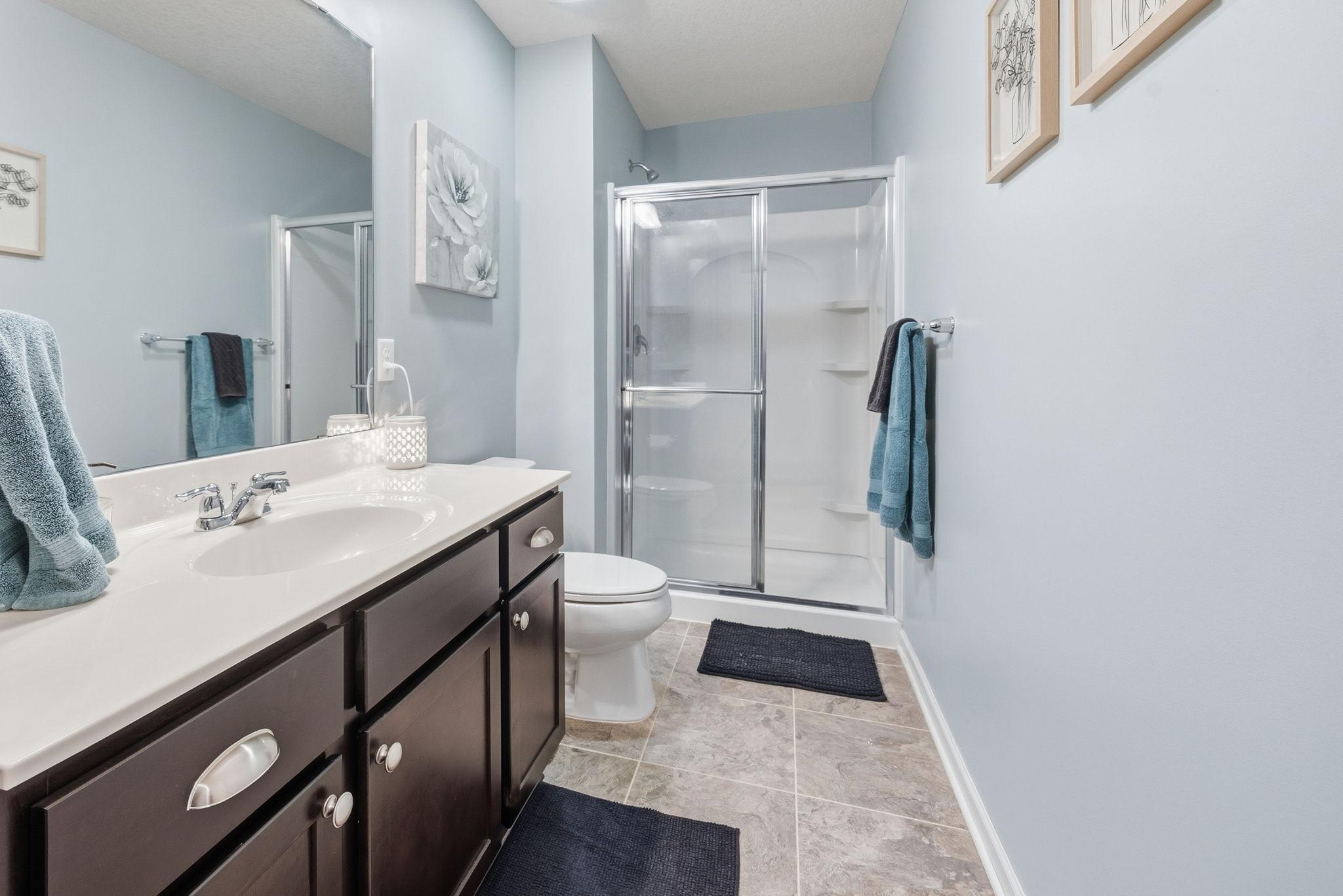 Finished lower-level bathroom with walk-in shower, oversized vanity, and neutral finishes provides added convenience for guests and entertaining.
