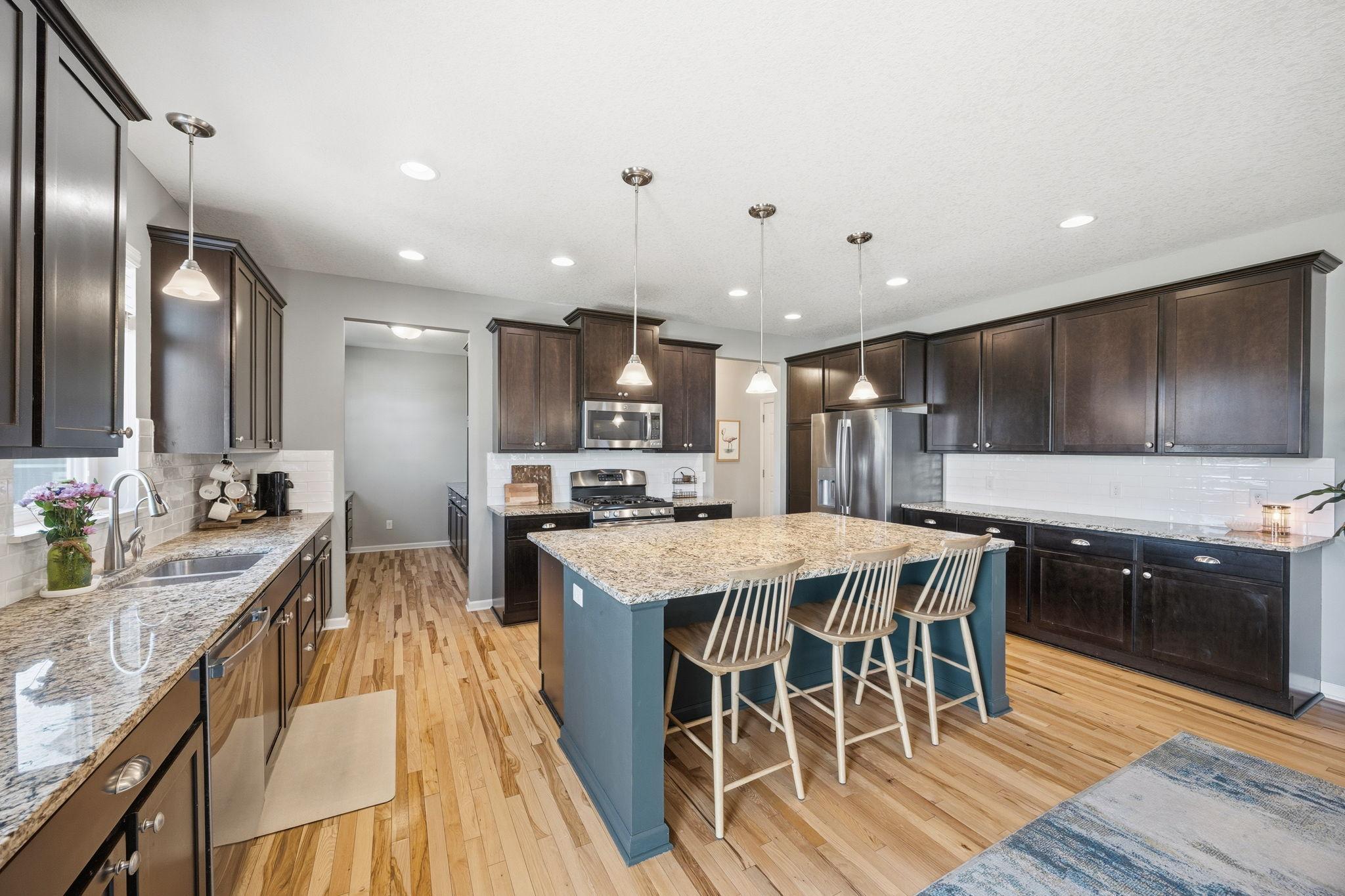 Spacious open-concept kitchen featuring oversized center island, granite countertops, rich cabinetry, stainless steel appliances, and abundant prep and storage space perfect for entertaining.