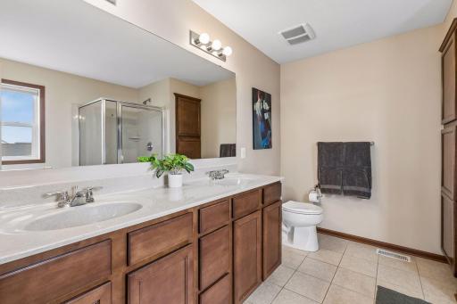 Spacious primary bath has dual sinks on a large vanity and a linen cabinet for storage.