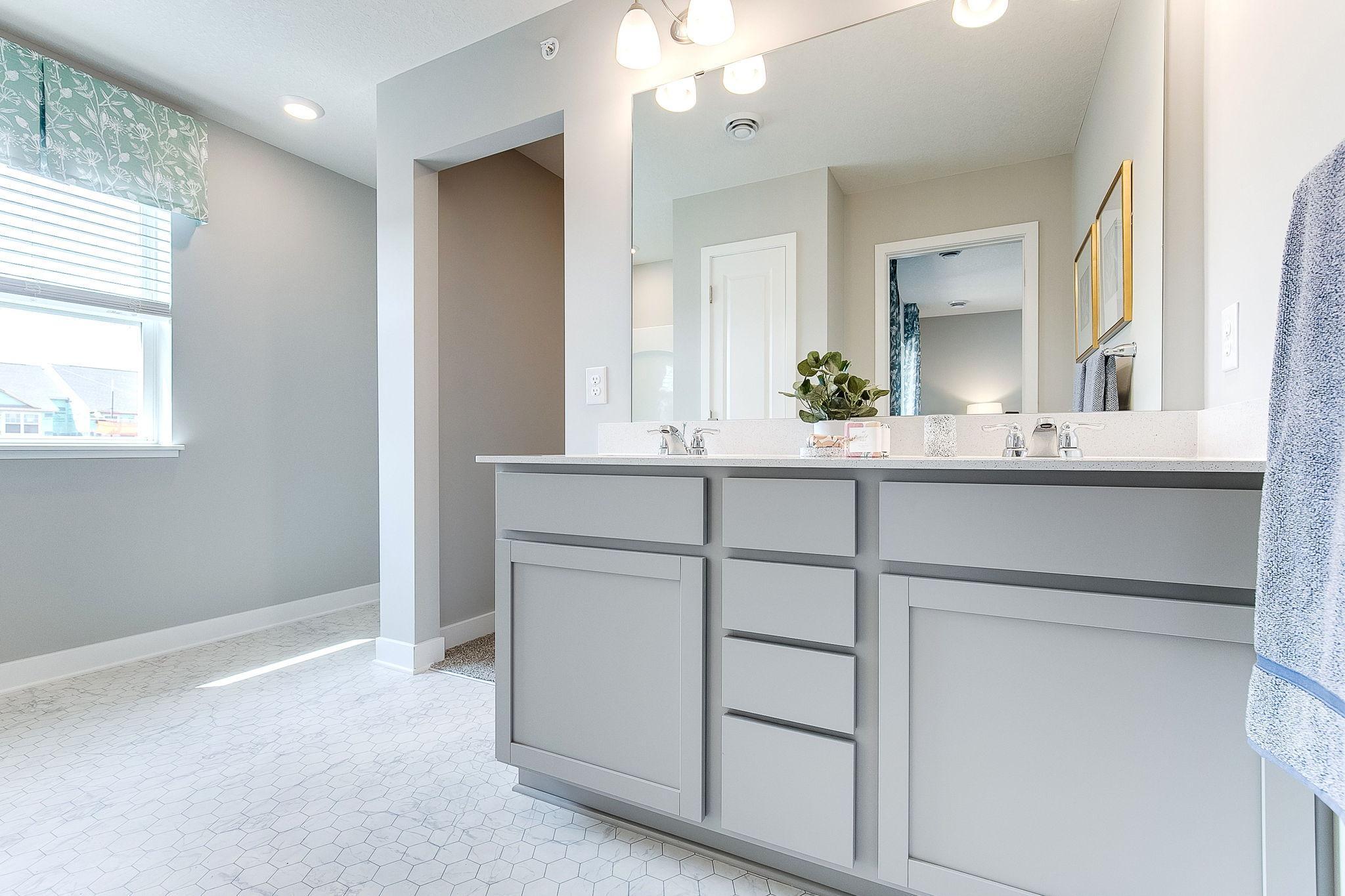 Primary bath with dual sinks, walk-in shower and large walk-in closet. Model photo. Options and colors will vary.