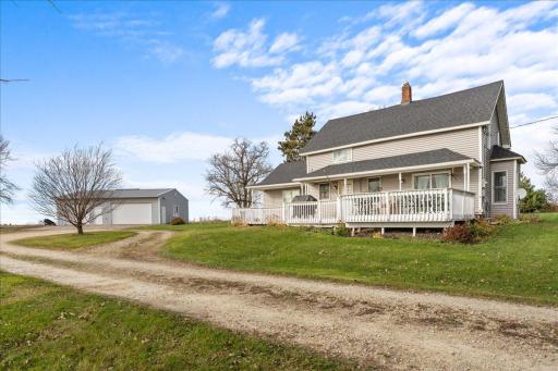 A charming farmhouse with a large porch sits peacefully on five sprawling acres beneath wide open skies.jpg