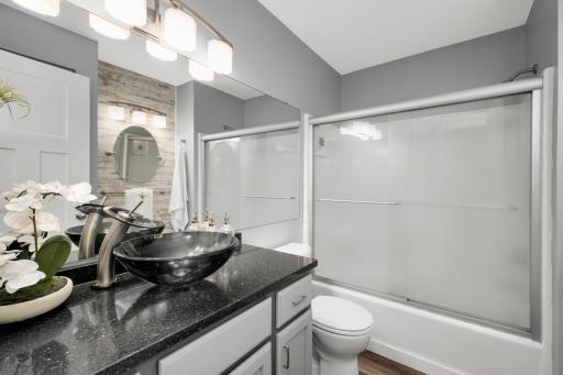 This stylishly updated bathroom has a modern, spa-like aesthetic. The space showcases a sleek black granite vanity countertop paired with a contemporary black vessel sink and brushed nickel waterfall faucet, creating a bold and elegance feel.
