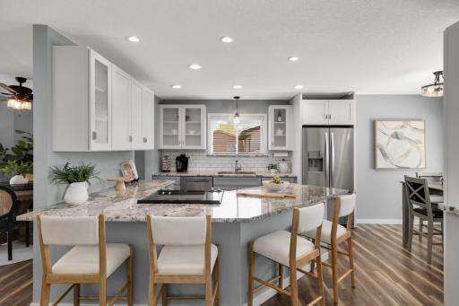 The kitchen has been tastefully updated with white cabinetry, granite-style countertops, stainless steel appliances, subway tile backsplash, and a large breakfast bar seating