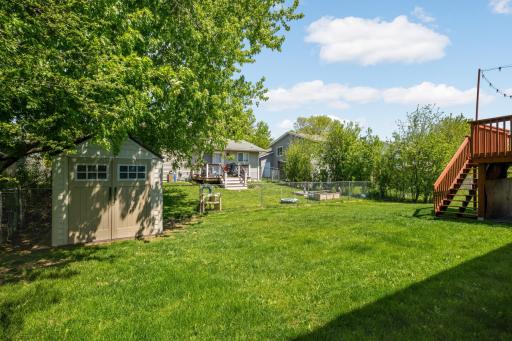 A fully fenced backyard with lush green grass and mature trees that provide both shade and privacy. The large yard offers plenty of room for entertaining, pets. gardening or any other outdoor activity + a shed for extra storage!