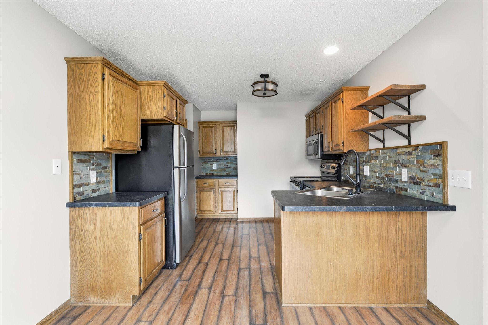 Open kitchen design features breakfast bar seating, updated fixtures, and modern open shelving accents.