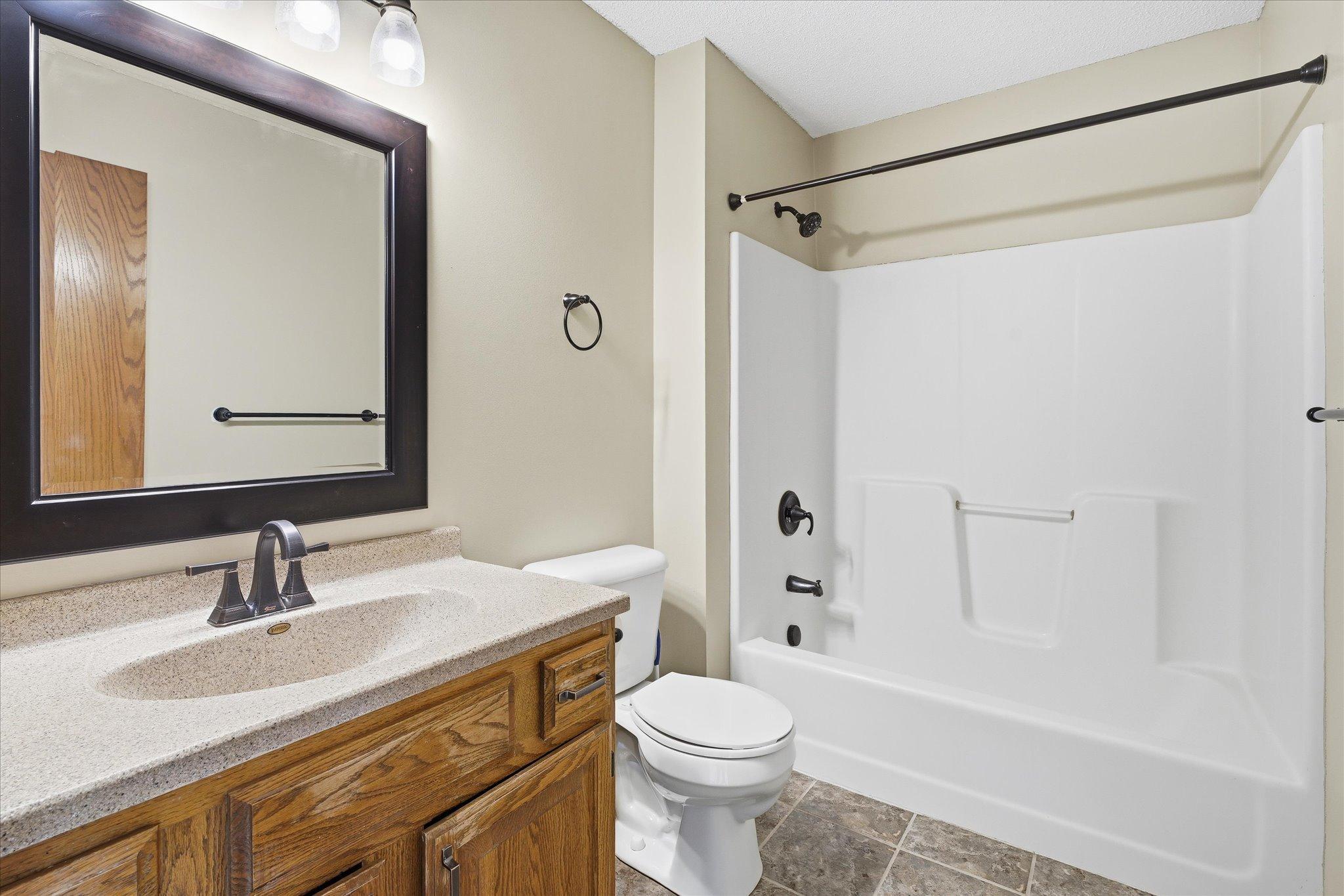 Updated private primary full bathroom with modern fixtures, stylish Corian counter top vanity, tiled floors, and easy-maintenance finishes.