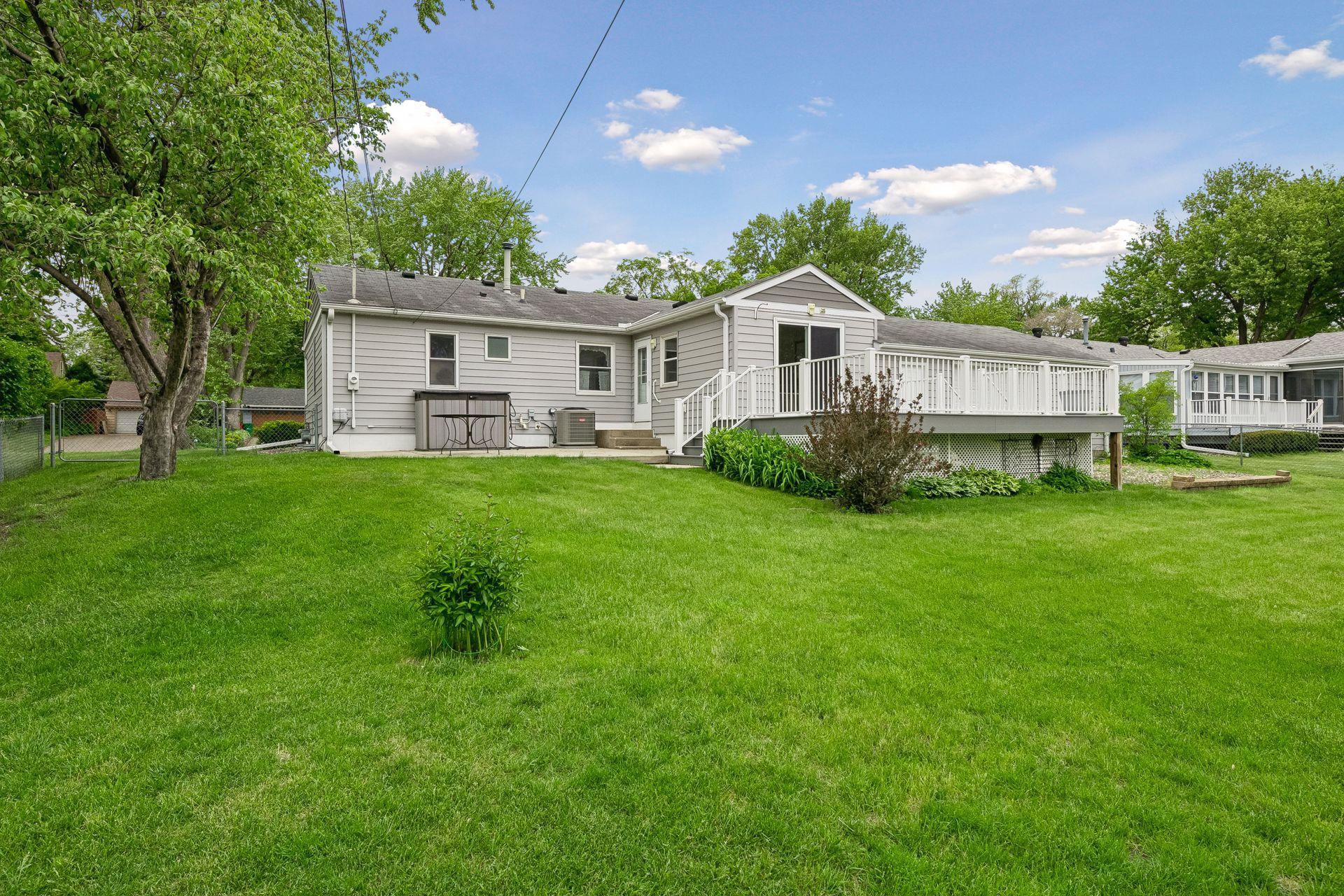 View of the back of the home - enjoy the deck, patio, flat yard, gardens and fenced yard