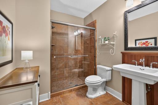 3/4 bathroom features charming pedestal sink with Redwood paneled backsplash, ceramic tile heated flooring and large shower features tile surround and glass doors