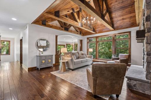 Your view from the front door. Dramatic timber trusses crafted from reclaimed century-old Wisconsin beams create a stunning focal point. Expansive windows fill the great room with natural light, blending warmth, character, and timeless craftsmanship.