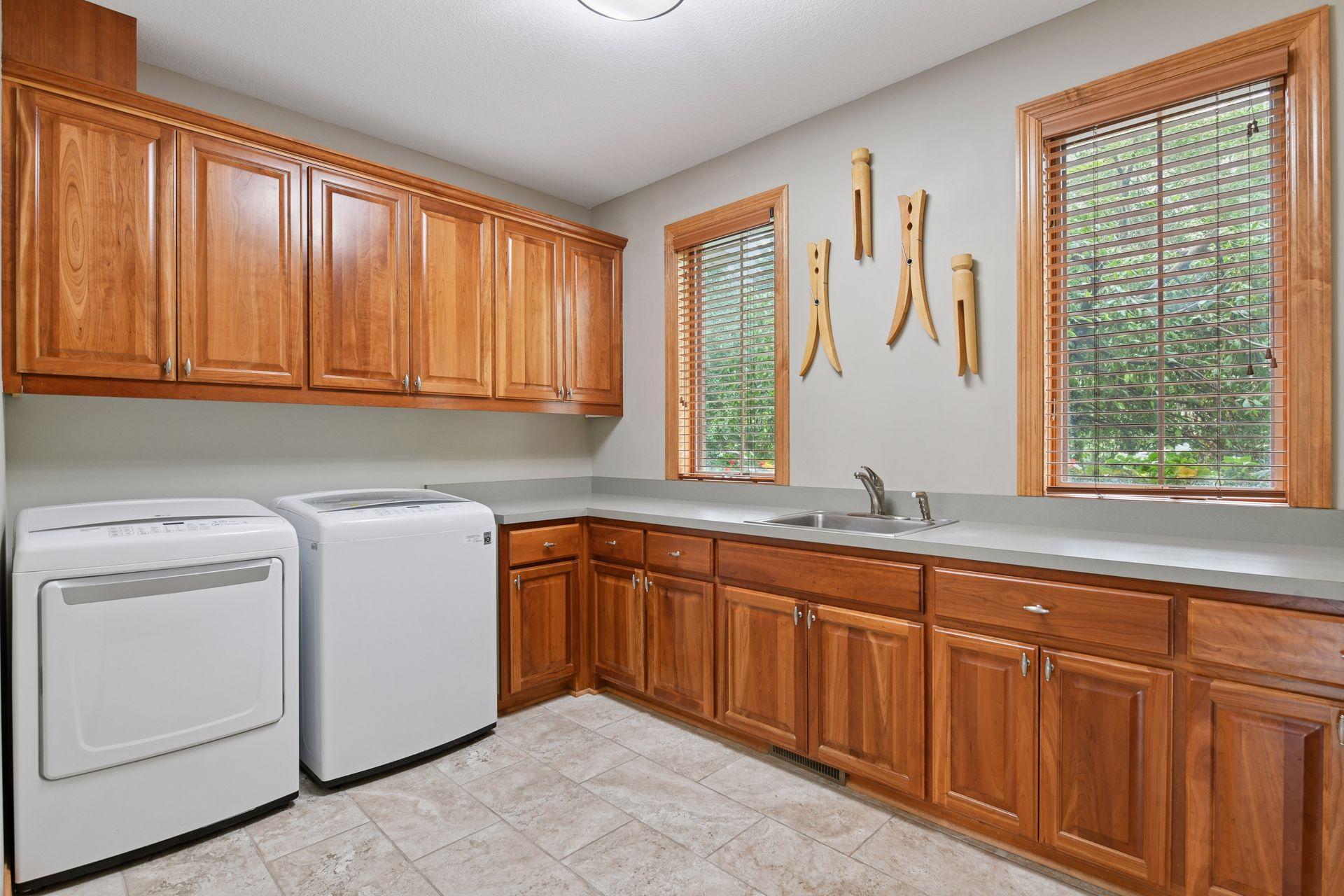 Huge laundry room includes washer, dryer, and sink with upper and lower cherry cabinetry.
