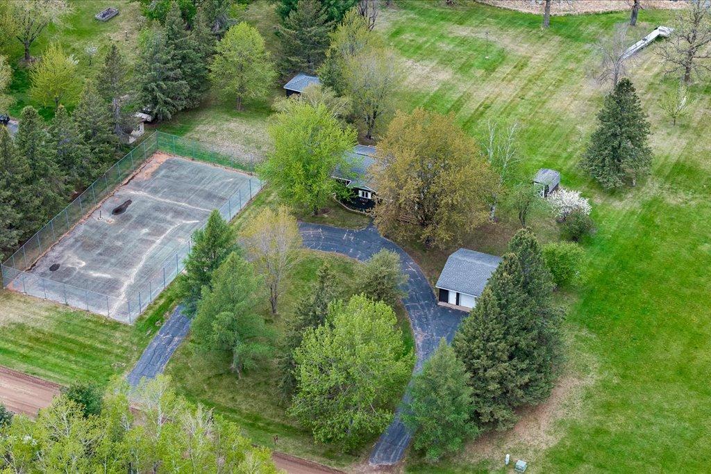 Aerial view of land showcasing tennis courts, detached garage, driveway, and 2 sheds