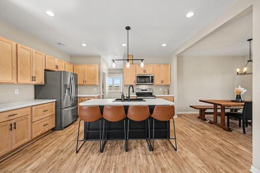 Open kitchen with dark center island, maple cabinetry, stainless steel appliances, and luxury vinyl plank flooring.