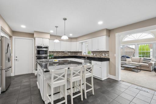 This clean and functional kitchen offers a timeless design with white cabinetry, granite countertops, and tile backsplash. A center island with seating serves as the perfect spot for casual dining or gathering.