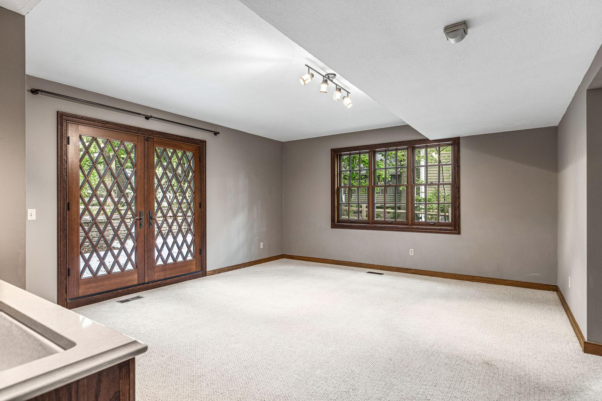Light-filled walkout lower level amusement room with distinctive French doors, oversized windows and flexible space for a game area or entertaining.