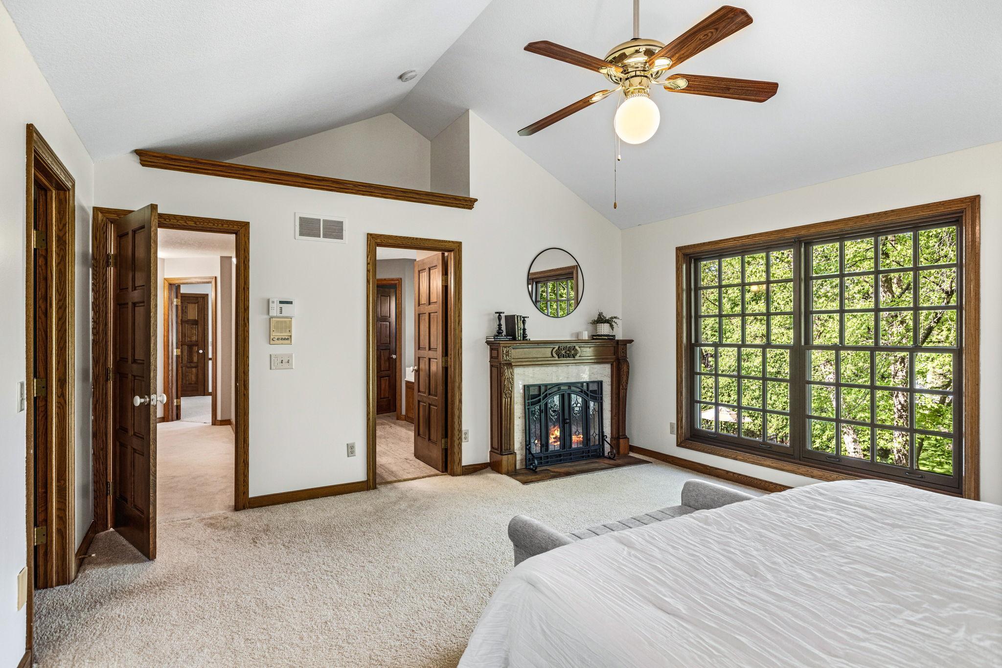 Another view of primary bedroom showing cozy fireplace and entrance to private, full bath.
