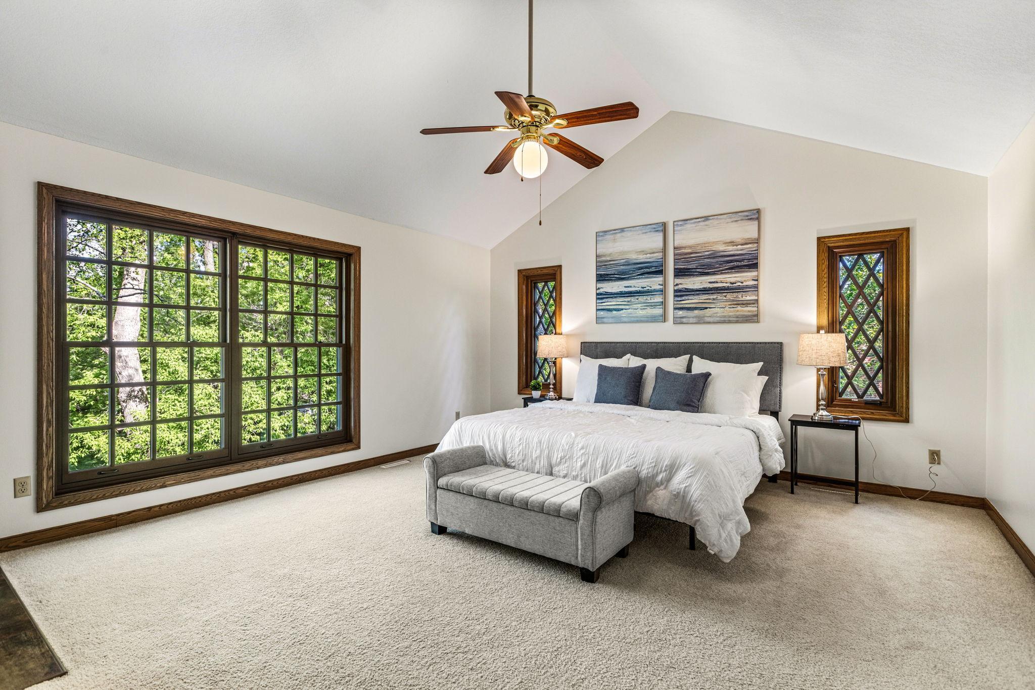 Spacious primary suite featuring vaulted ceilings and oversized windows that fill the room with natural light and peaceful wooded views.