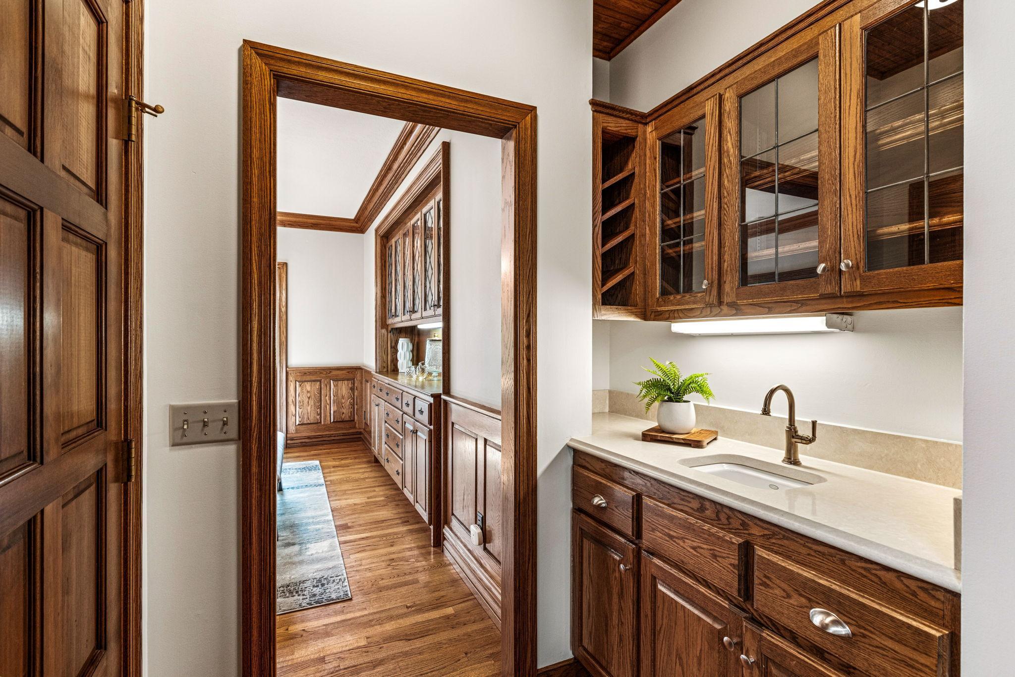Convenient butler pantry with sink and glass-front cabinetry offers the perfect space when entertaining. Rich woodwork, custom millwork and hardwood floors continue throughout the home, adding timeless character and warmth.