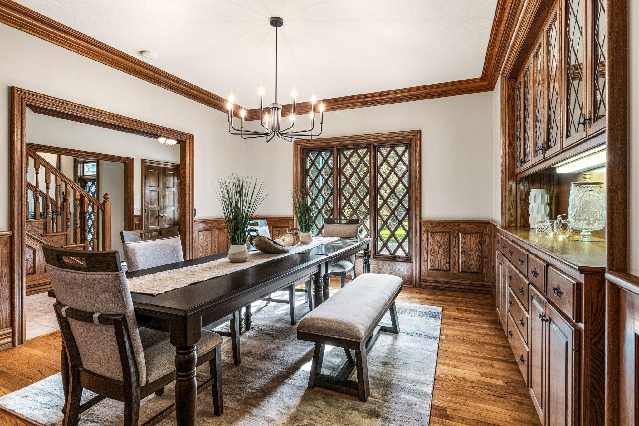 Elegant formal dining room featuring rich hardwood floors, detailed millwork and a stunning built-in buffet with leaded glass cabinetry. The beautiful diamond-pane windows add timeless character and charm to this inviting entertaining space.