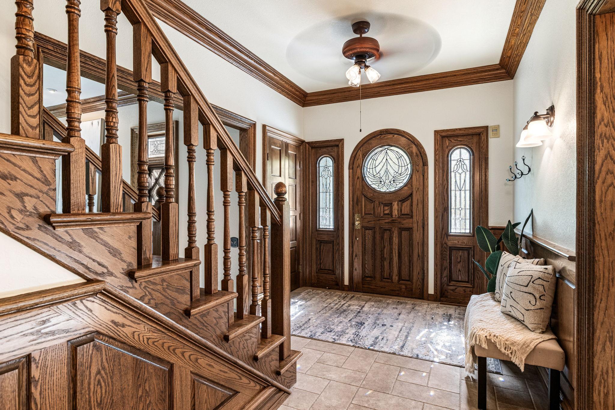 Impressive foyer showcasing rich oak woodwork, custom staircase and stunning leaded glass entry door - setting the tone for the timeless craftsmanship found throughout the home.