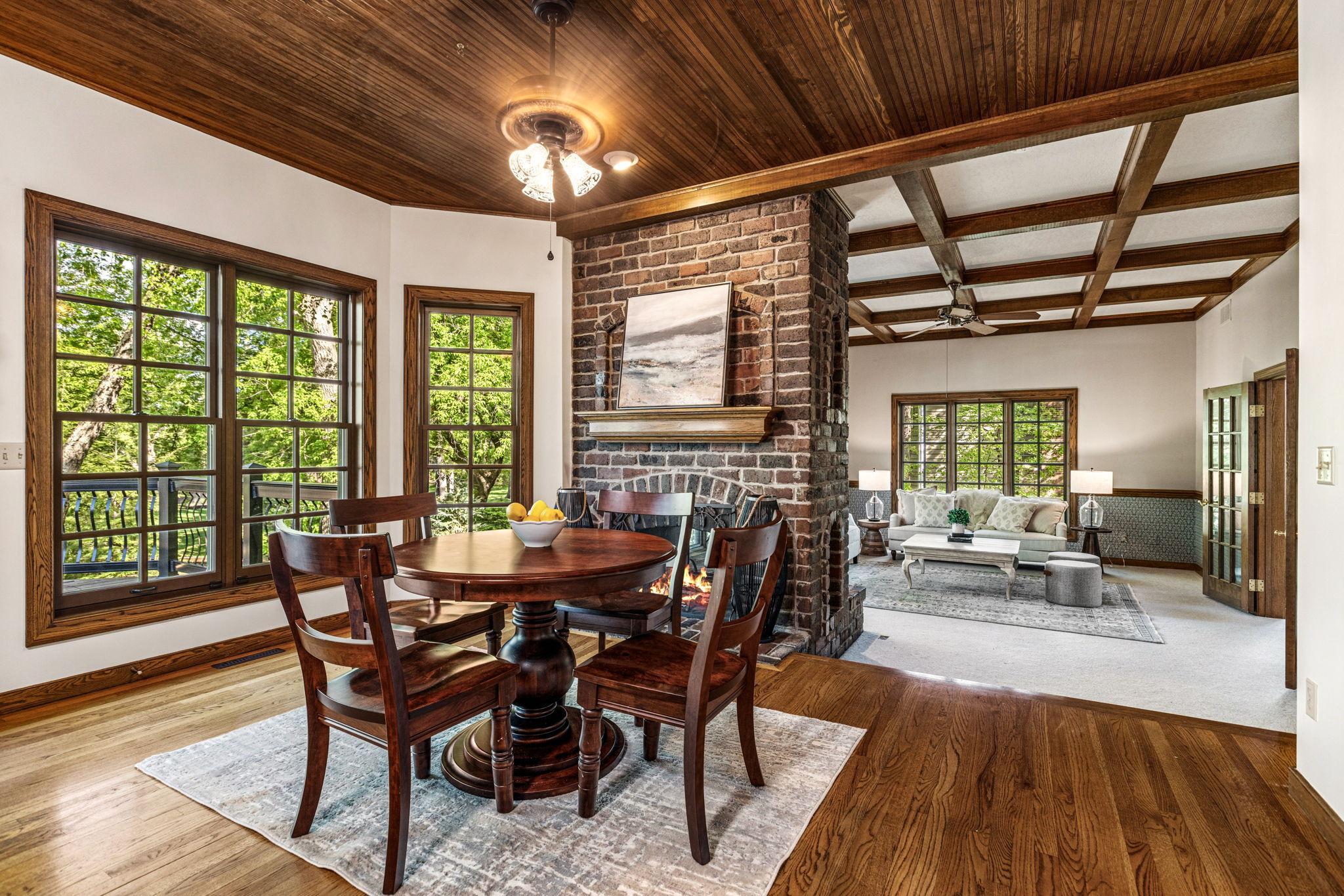 Charming informal dining area with rich hardwood floors, dramatic beadboard ceiling and a striking double-sided brick fireplace that creates warmth and character throughout the space.