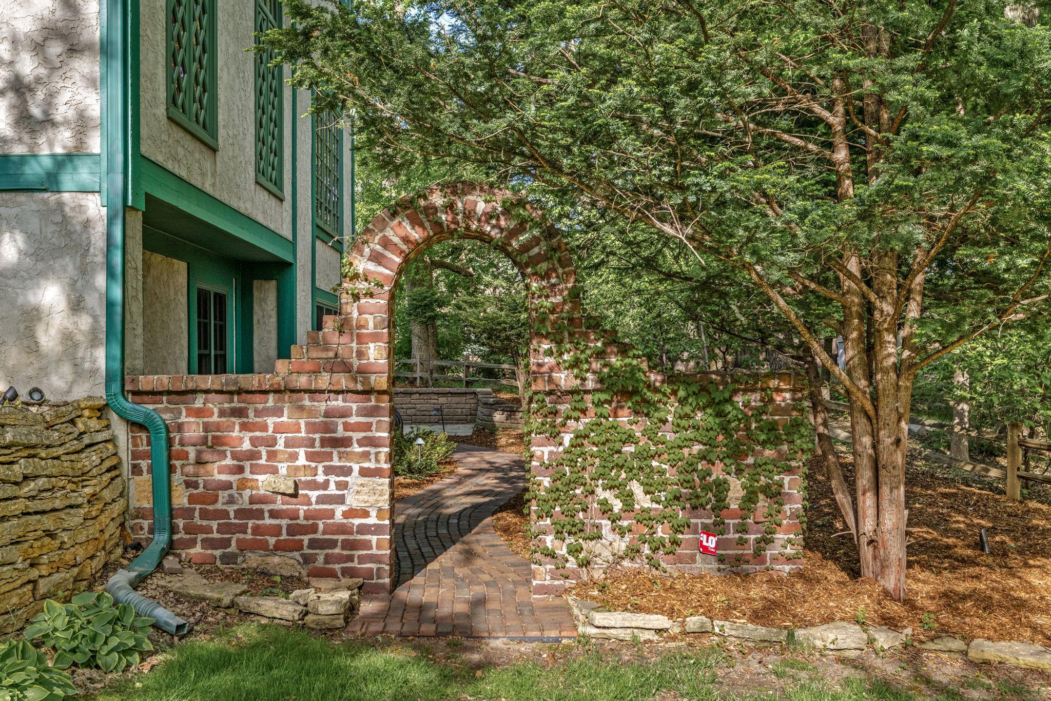 Storybook brick archway and winding paver paths add timeless charm to this enchanting backyard retreat.