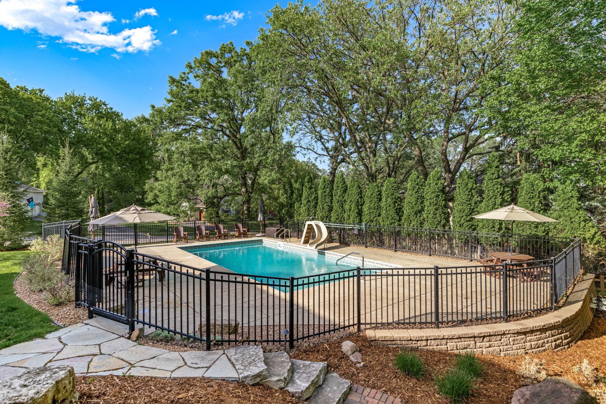 Resort-style backyard featuring an in-ground pool surrounded by mature trees, expansive patio spaces and lush privacy landscaping - an incredible setting for summer entertaining and everyday relaxation.