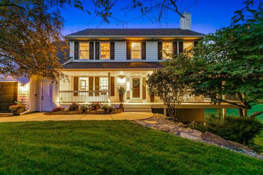 Beautiful curb appeal at dusk, with a welcoming covered front porch, mature trees and lush landscaping creating a peaceful country-home setting.