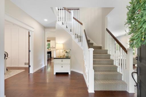Welcoming foyer featuring rich hardwood floors, crisp white millwork, and an open staircase—setting a warm, elegant tone from the moment you enter.